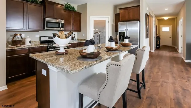 a kitchen with granite countertop kitchen island stainless steel appliances a sink counter space and wooden floor