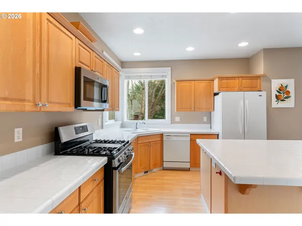 a kitchen with stainless steel appliances granite countertop a stove top oven a sink a refrigerator and white cabinets with wooden floor
