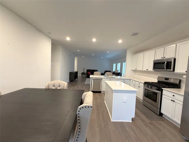 a large kitchen with stainless steel appliances granite countertop a stove a sink a refrigerator and white cabinets with wooden floor