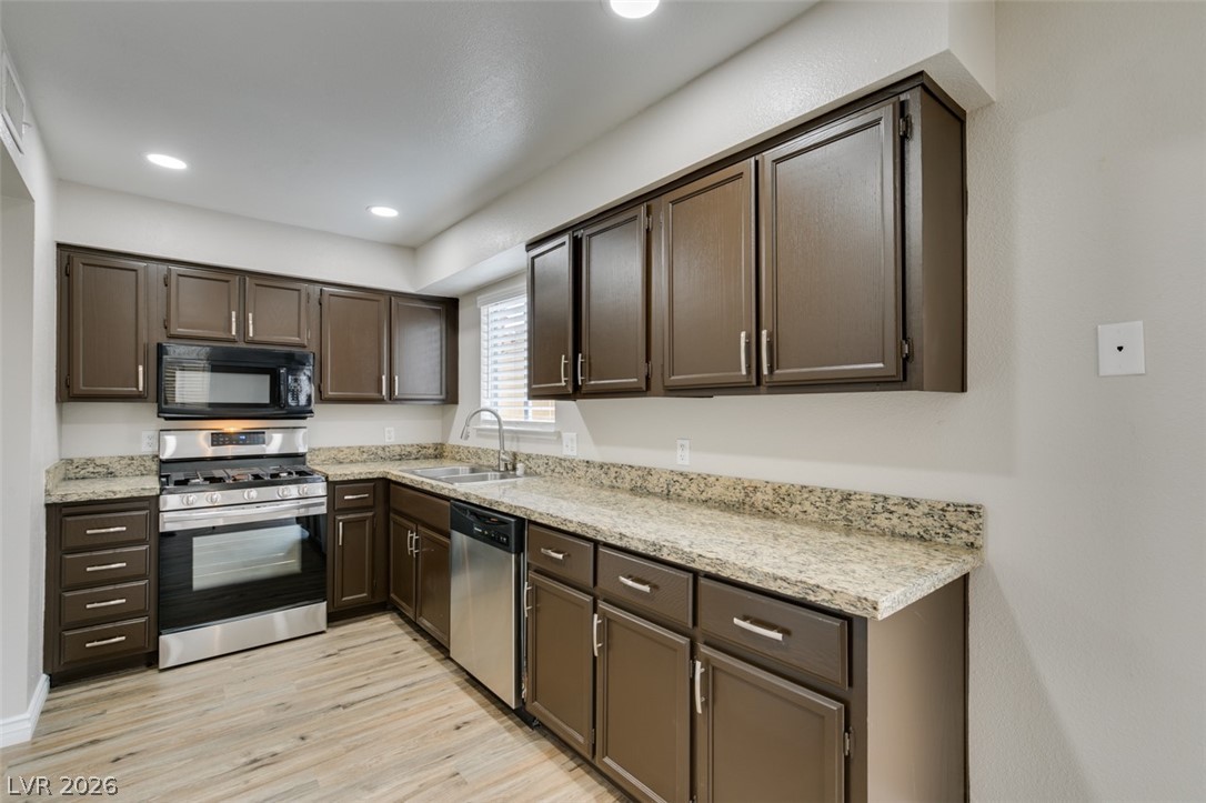 905 Scarlet Ridge Drive Las Vegas, NV 89128 - Photo 17 of 39 Kitchen featuring stainless steel appliances, dark wood finish cabinets, light wood finished floors, light stone counters, and recessed lighting