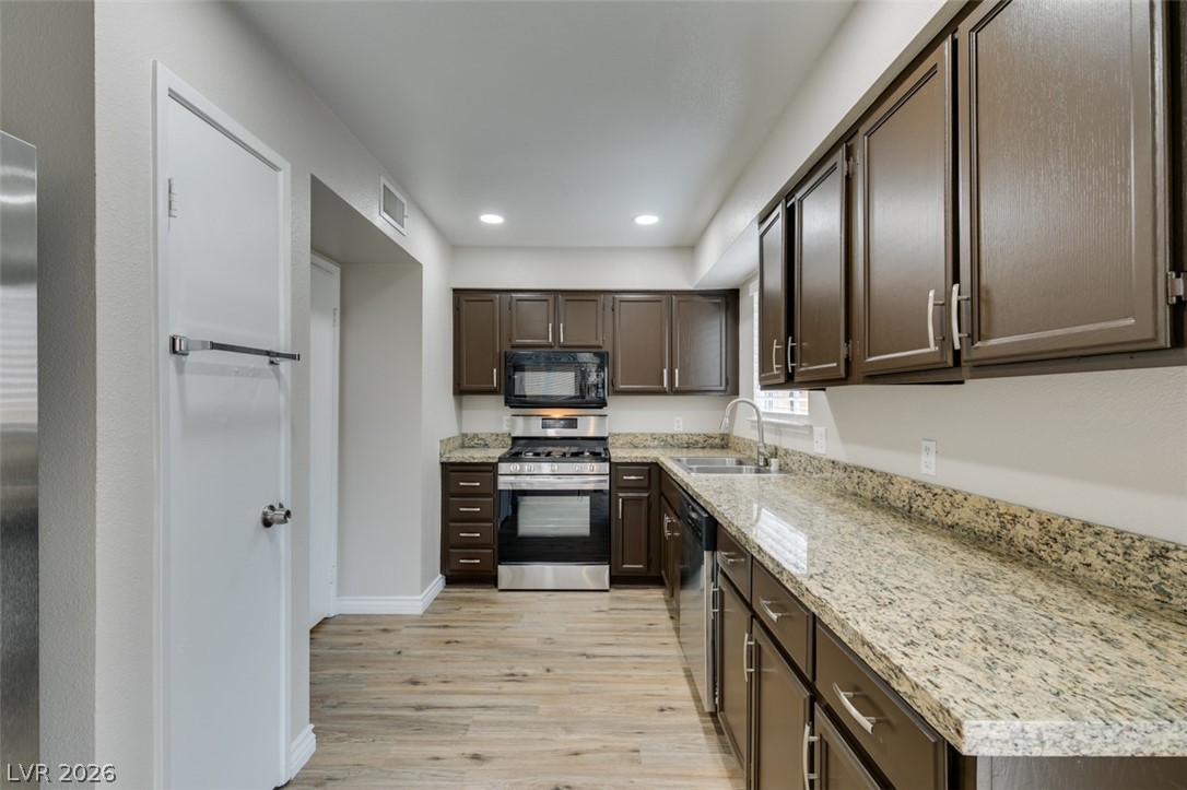 905 Scarlet Ridge Drive Las Vegas, NV 89128 - Photo 18 of 39 Kitchen with dark wood finish cabinets, stainless steel appliances, light wood finished floors, light stone countertops, and recessed lighting
