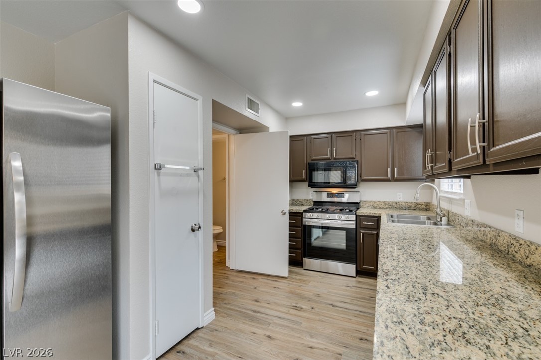 905 Scarlet Ridge Drive Las Vegas, NV 89128 - Photo 20 of 39 Kitchen with stainless steel appliances, dark wood finish cabinets, light stone countertops, light wood-type flooring, and recessed lighting