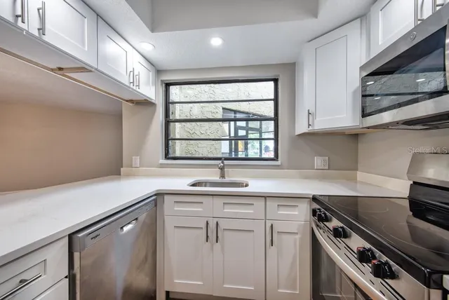 a kitchen with white cabinets appliances a sink and a window