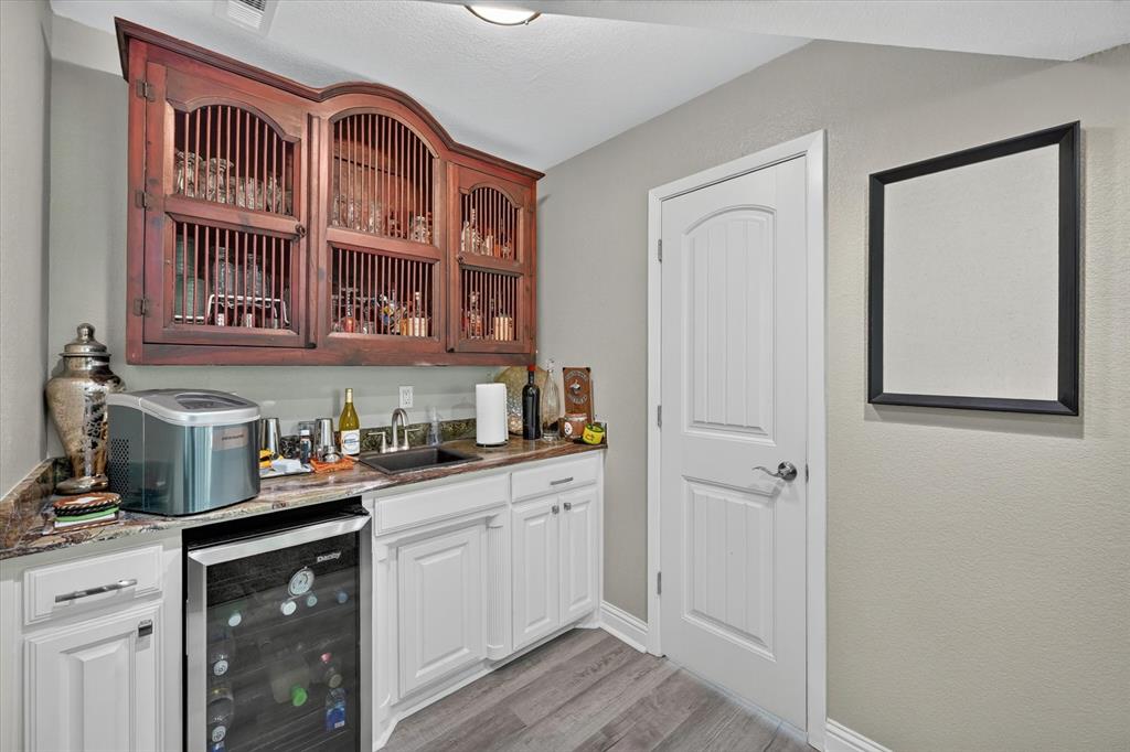 47 Bounty Road East Benbrook, TX 76132 - Photo 13 of 39 Custom bar area featuring dark wood upper cabinetry with slatted doors, a granite countertop, and a built-in beverage refrigerator