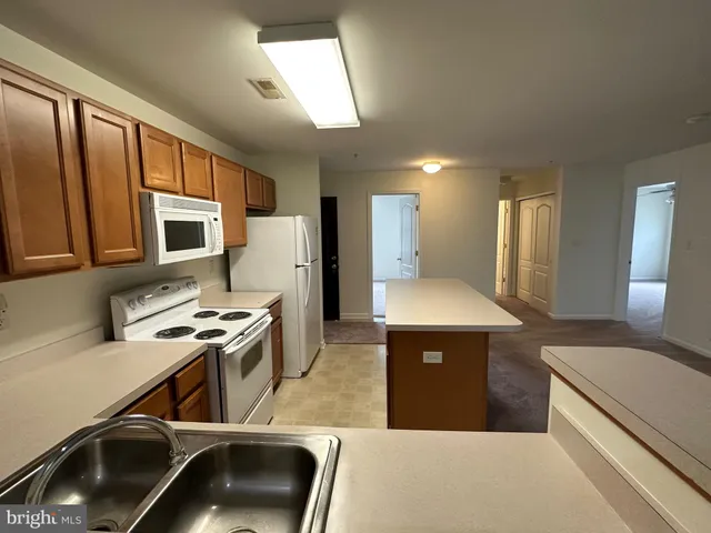 a large kitchen with stainless steel appliances a large counter top a stove a microwave a sink a refrigerator and white cabinets