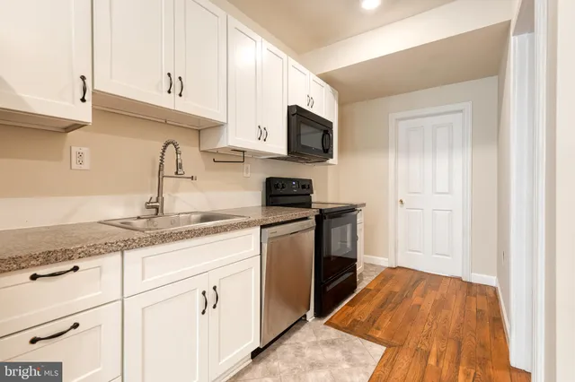 a kitchen with granite countertop a sink dishwasher stove and white cabinets with wooden floor