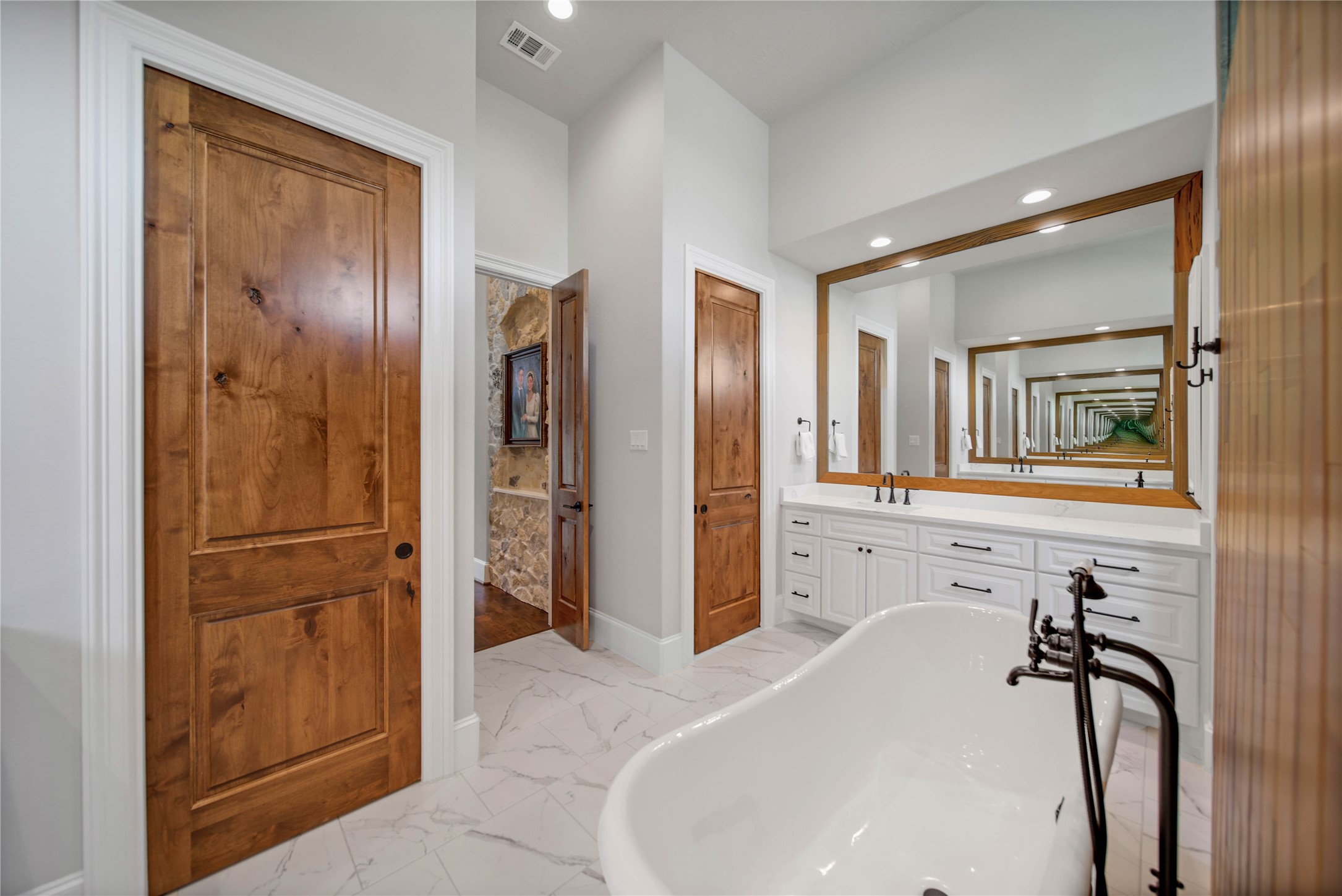 24718 Shadow Pond Spring, TX 77389 - Photo 24 of 49 Luxurious bathroom featuring a freestanding clawfoot tub, elegant wood doors, and a spacious double vanity with a large mirror, creating a serene and inviting atmosphere.