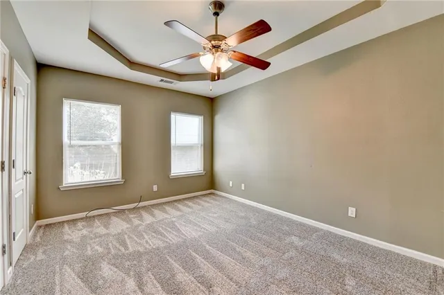 an empty room with chandelier fan and windows
