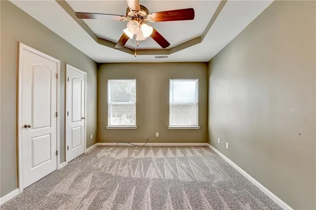 an empty room with chandelier fan and windows
