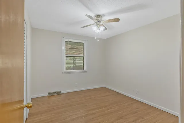 an empty room with wooden floor chandelier fan and windows