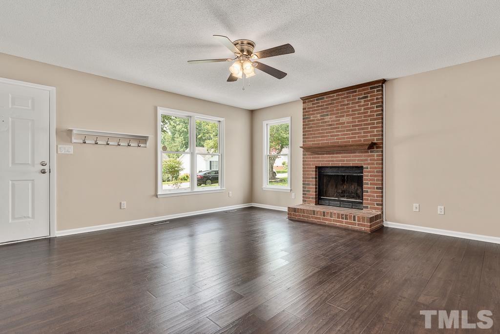 3308 Castlegate Drive Raleigh, NC 27616 - Photo 2 of 22 an empty room with wooden floor a fireplace a ceiling fan and windows