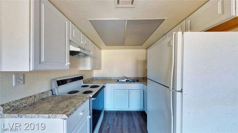 6213 Smoke Ranch Road Las Vegas, NV 89108 - Photo 21 of 22 Kitchen with white appliances, white cabinetry, under cabinet range hood, light countertops, and dark wood-type flooring