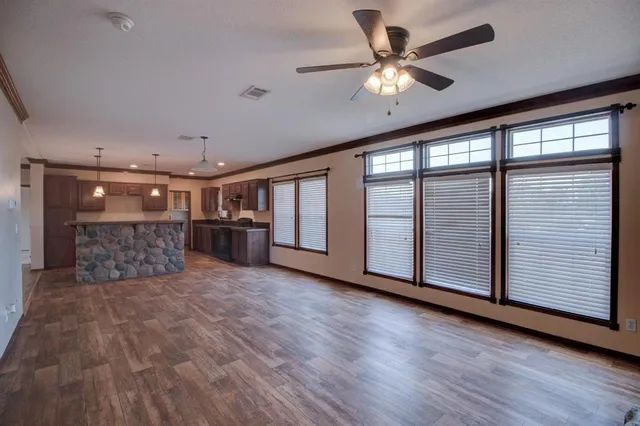 a big room with wooden floor a ceiling fan and windows