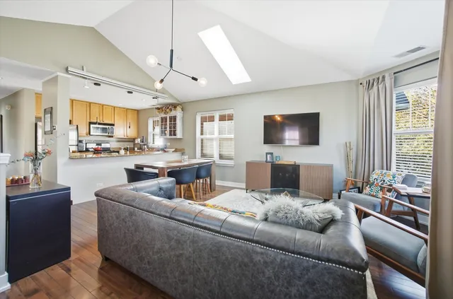 a living room with stainless steel appliances kitchen island granite countertop a dining table chairs and a refrigerator