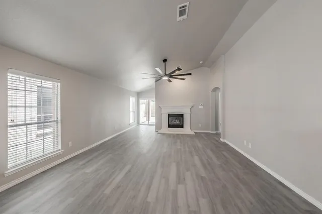 an empty room with wooden floor ceiling fan and windows