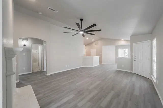 a view of an empty room with wooden floor and a ceiling fan