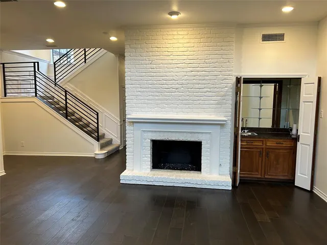 a view of an empty room with wooden floor fire place and windows