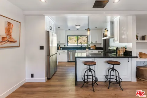a kitchen with stainless steel appliances kitchen island granite countertop a stove a refrigerator a sink a dining table and chairs with wooden floor