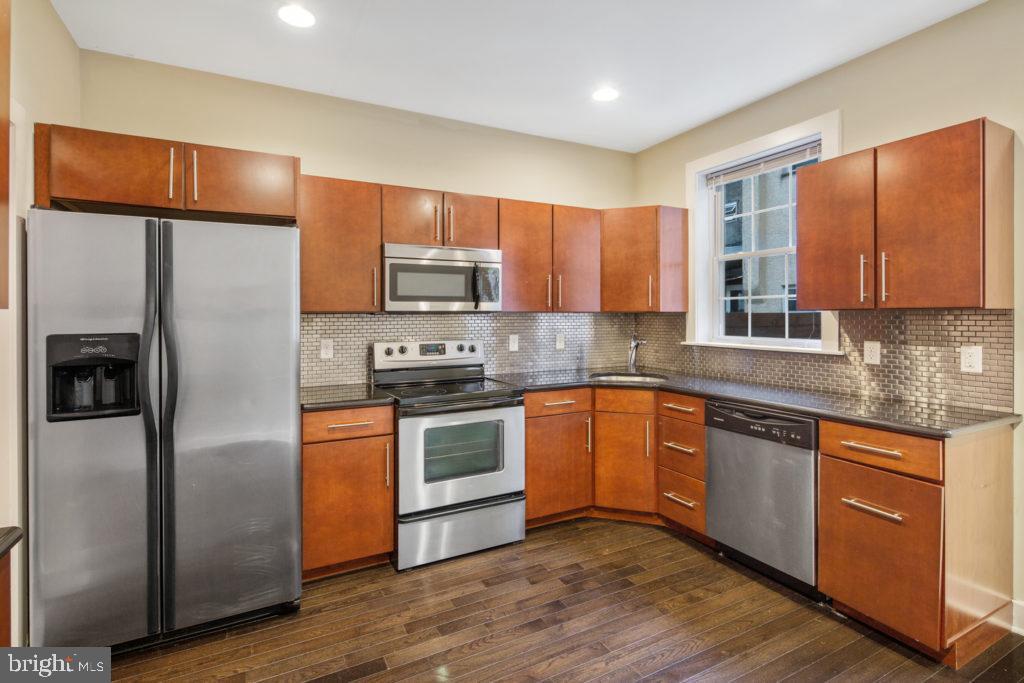 a kitchen with stainless steel appliances granite countertop wooden cabinets a refrigerator a sink a stove a microwave and wooden floors