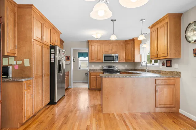 a kitchen with stainless steel appliances granite countertop a refrigerator a sink dishwasher a stove and white countertops with wooden floor