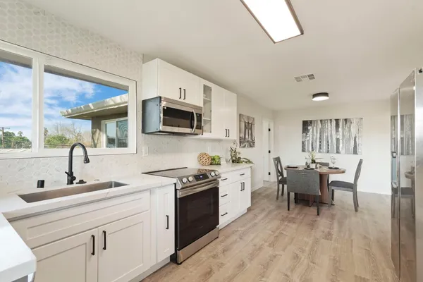 a kitchen with stainless steel appliances kitchen island granite countertop a sink dishwasher stove and white cabinets with wooden floor