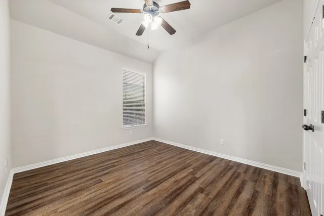 a view of an empty room with wooden floor and a ceiling fan