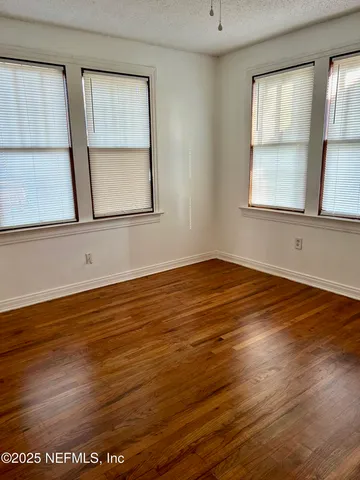a view of an empty room with wooden floor and window