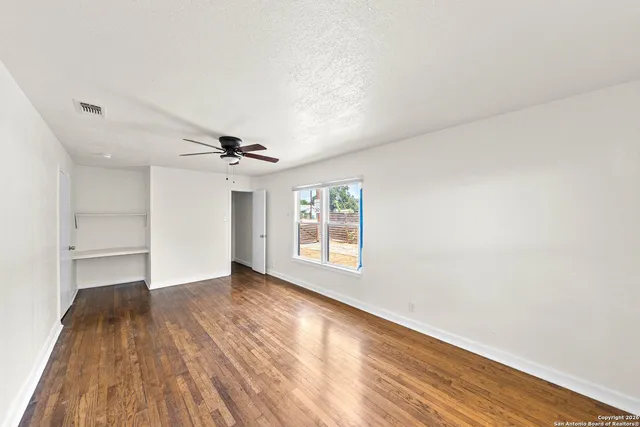 an empty room with wooden floor ceiling fan and windows