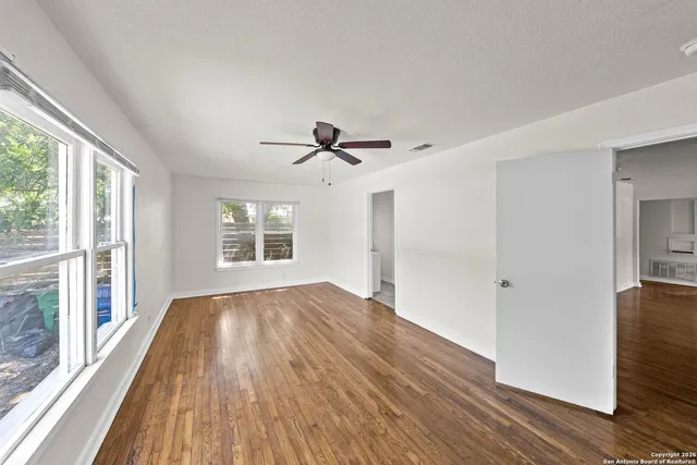 a view of empty room with wooden floor and fan