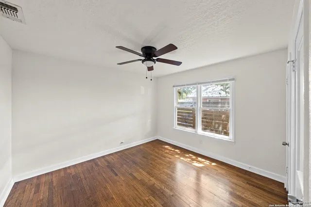 an empty room with wooden floor chandelier fan and windows