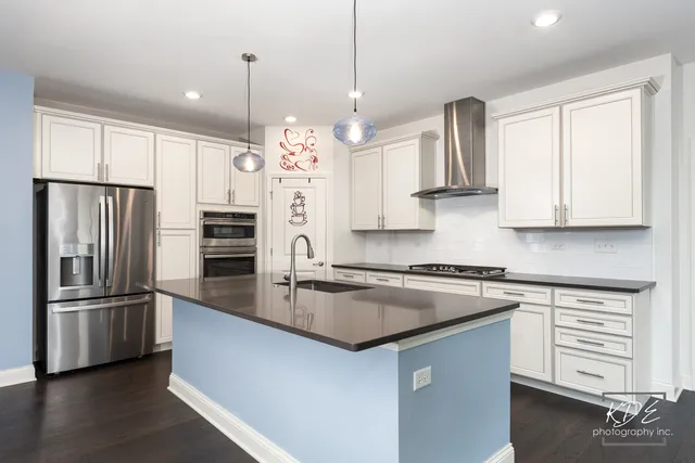 a kitchen with stainless steel appliances granite countertop a refrigerator a sink dishwasher a stove and white cabinets with wooden floor