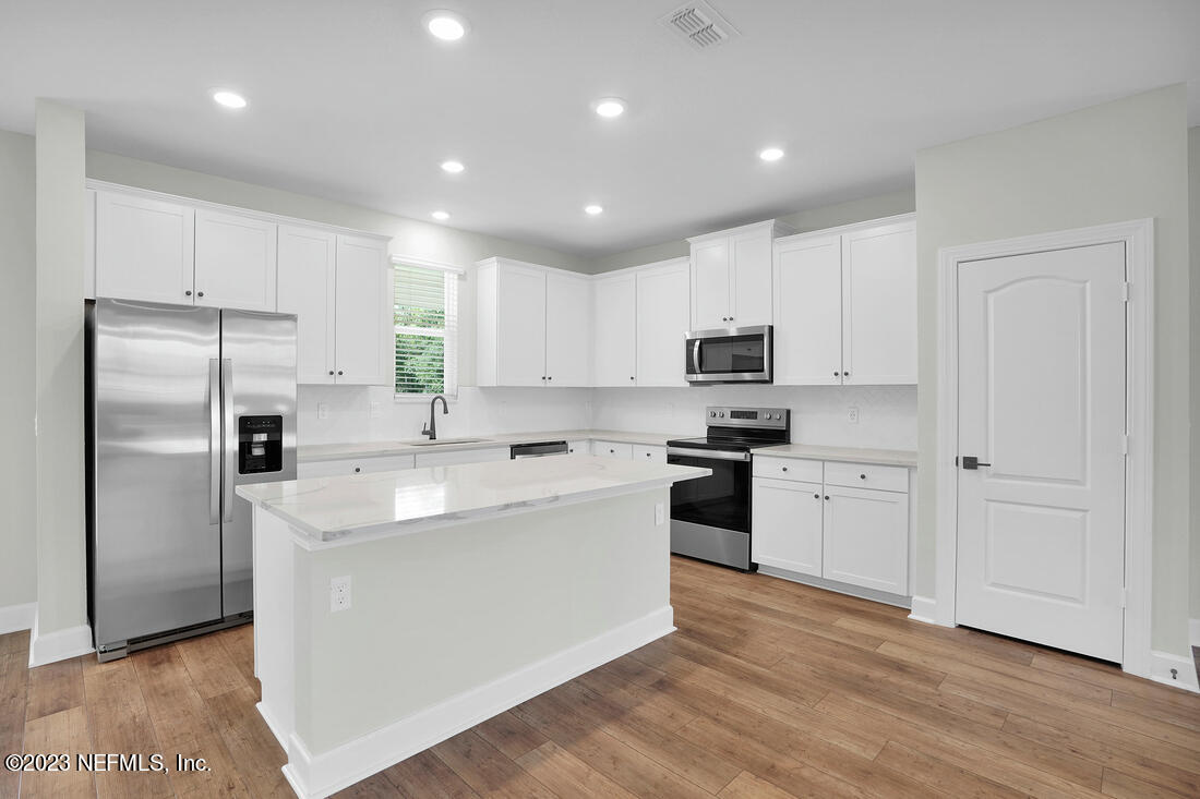 1074 Morgans Treasure Road St. Augustine, FL 32084 - Photo 2 of 11 a large kitchen with stainless steel appliances granite countertop a stove a sink a refrigerator and white cabinets with wooden floor