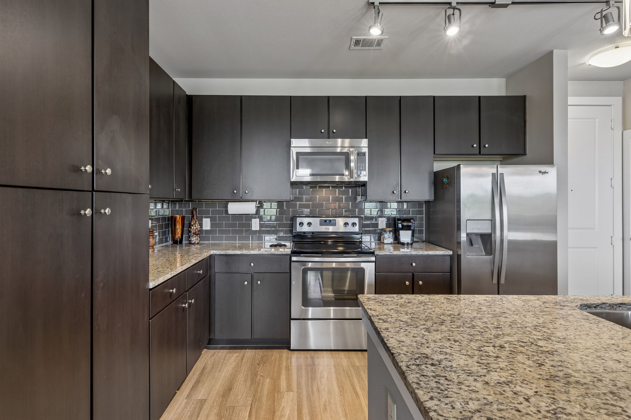 1900 Barton Springs Road, Unit 5032 Austin, TX 78704 - Photo 6 of 40 Kitchen featuring dark wood-finish cabinetry with silver hardware, light wood-finish flooring, full suite of stainless steel appliances, speckled granite countertops, and a subway tile backsplash