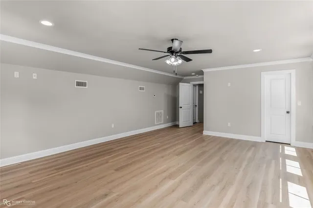 a view of an empty room with wooden floor and a ceiling fan