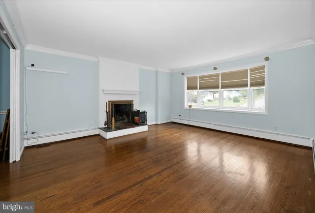 an empty room with wooden floor fireplace and windows