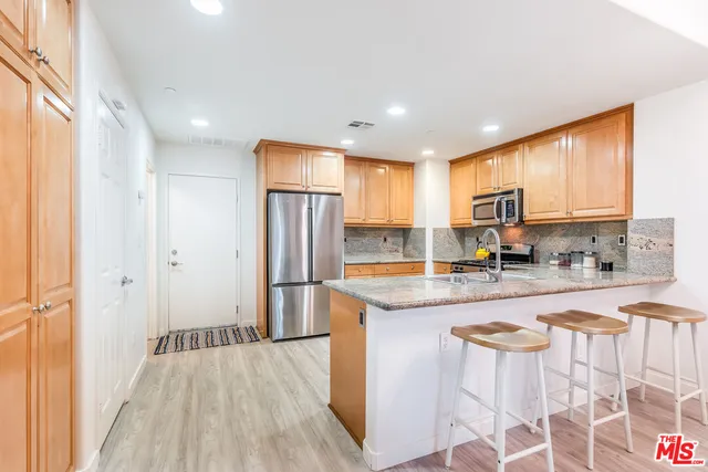 a kitchen with stainless steel appliances granite countertop a refrigerator a sink dishwasher a stove and white countertops with wooden floor