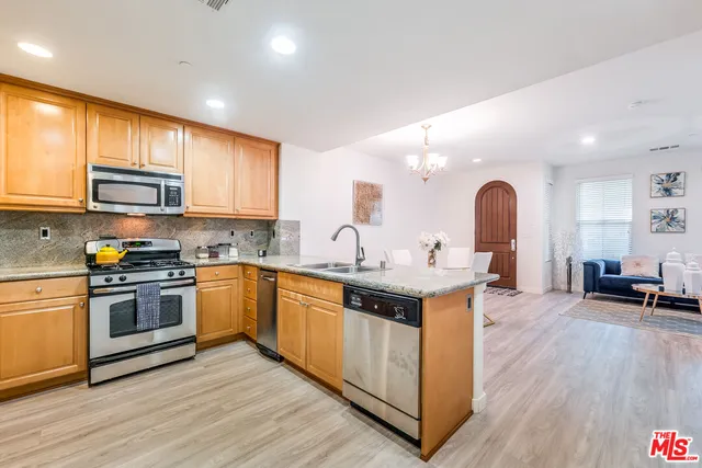 a kitchen with stainless steel appliances granite countertop a stove top oven a sink a dining table and chairs with wooden floor