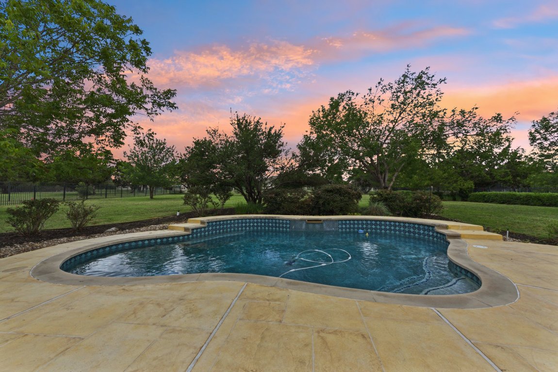 The in-ground pool is the centerpiece of the backyard oasis, surrounded by professional landscaping and open views that create a private resort-like setting.