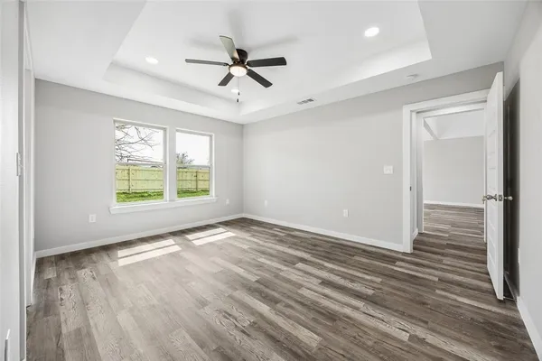 an empty room with wooden floor chandelier fan and windows