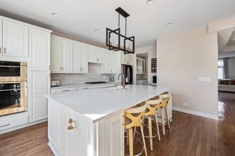 a kitchen with stainless steel appliances granite countertop a kitchen island a stove a sink a refrigerator white cabinets and wooden floor