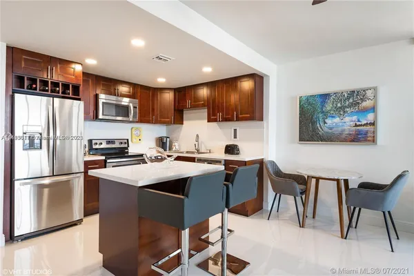 a kitchen with stainless steel appliances kitchen island granite countertop a refrigerator a stove a sink a dining table and chairs with wooden floor