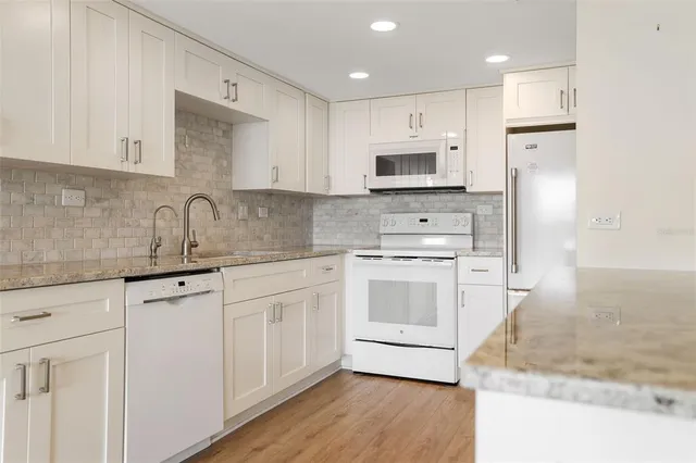 a kitchen with stainless steel appliances granite countertop a sink a stove a refrigerator and white cabinets