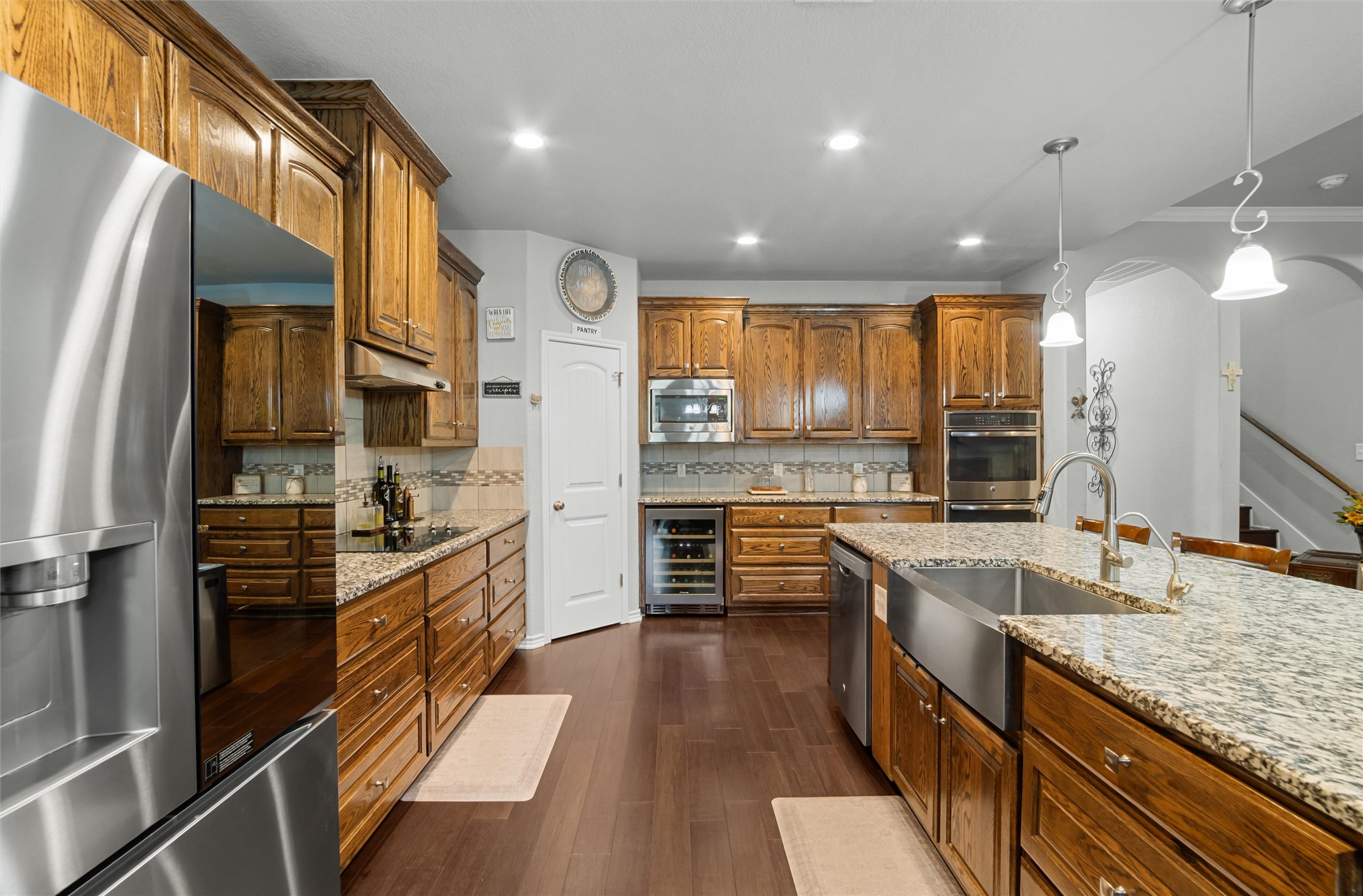 16017 Toby Court Temple, TX 76502 - Photo 10 of 33 Kitchen with appliances with stainless steel finishes, brown cabinetry, hanging light fixtures, dark wood finished floors, and wine cooler