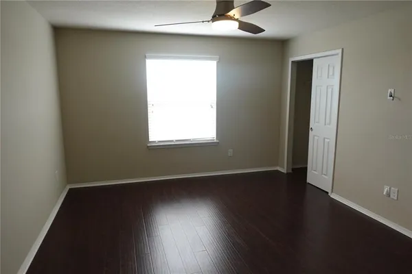 an empty room with wooden floor chandelier fan and windows