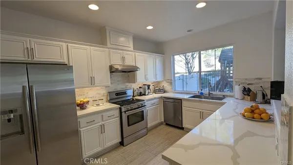 a kitchen with granite countertop stainless steel appliances a sink a stove a refrigerator cabinets and a window