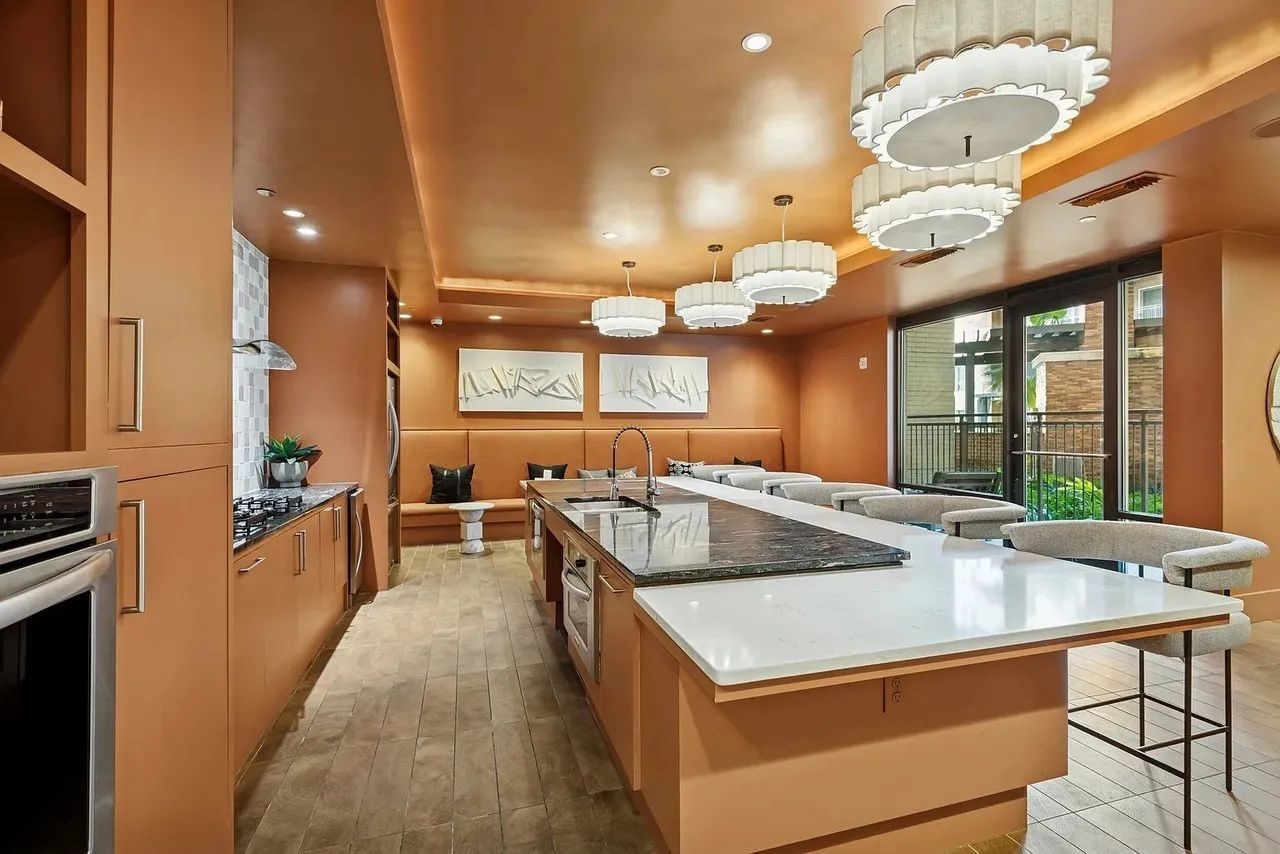 2724 Kipling Street, Unit 535 Houston, TX 77098 - Photo 6 of 30 The wine and dine area wrapped in a monolithic terracotta "color-drench," this space creates a sophisticated, social cocoon. The warm, immersive palette is punctuated by a rhythmic line of scalloped chandeliers that soften the room's sharp linear geometry. It’s a masterclass in atmospheric design—blending the intimacy of a private lounge with the professional scale of a grand culinary hub.