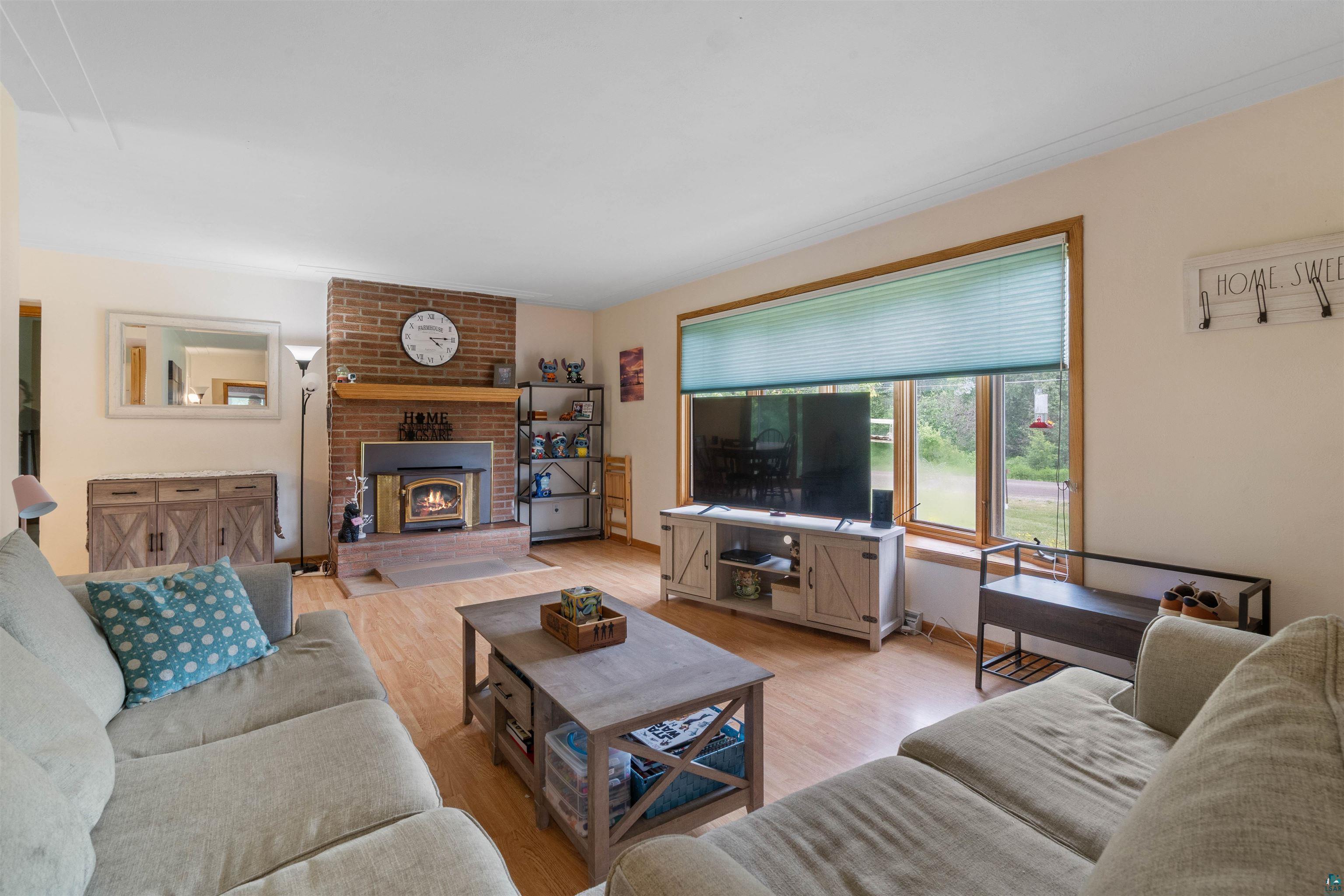 3711 Getchell Road Hermantown, MN 55811 - Photo 5 of 31 Living area featuring wood-finish flooring, a brick-surround fireplace with hearth, and a large window with natural wood trim