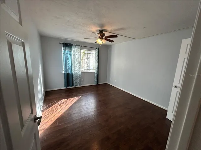 an empty room with wooden floor fan and windows