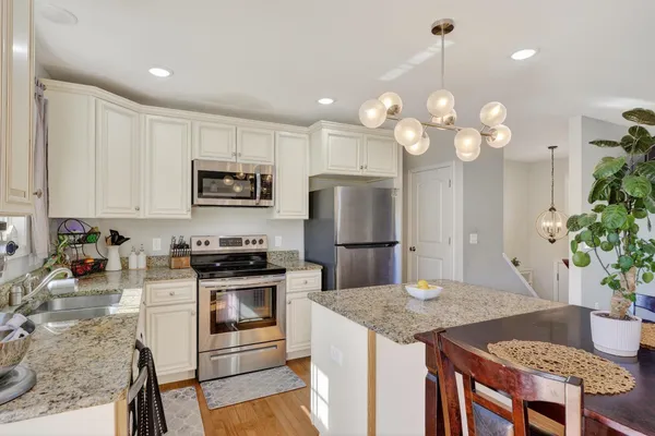 a kitchen with kitchen island granite countertop stainless steel appliances a sink a stove cabinets dining table and chairs