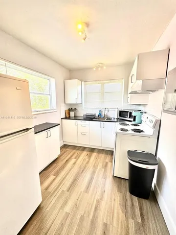 a living room with stainless steel appliances kitchen island granite countertop a stove a sink dishwasher and white cabinets with wooden floor